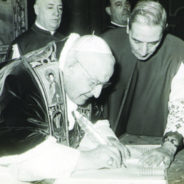 Palazzo Apostolico, Sala Clementina, 25 dicembre 1961. Giovanni XXIII sottoscrive la Bolla di indizione del Concilio ecumenico Vaticano II «Humanæ salutis», aiutato da mons. Enrico Dante, segretario della Congregazione dei Riti. Alle loro spalle (da sinistra) mons. Mario Nasalli Rocca di Corneliano, maestro di Camera (futuro cardinale), e mons. Canisio Van Lierde, Sacrista pontificio (foto ASV, Conc. Vat. II, b. 634, fasc. 3)