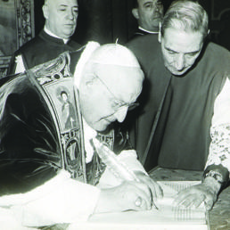 Palazzo Apostolico, Sala Clementina, 25 dicembre 1961. Giovanni XXIII sottoscrive la Bolla di indizione del Concilio ecumenico Vaticano II Human salutis, aiutato da mons. Enrico Dante, segretario della Congregazione dei Riti. Alle loro spalle (da sinistra) mons. Mario Nasalli Rocca di Corneliano, maestro di Camera (futuro cardinale), e mons. Canisio Van Lierde, Sacrista pontificio (foto ASV, Conc. Vat. II, b. 634, fasc. 3)