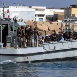 Un'imbarcazione trasborda un gruppo di migranti dal molo di Lampedusa alla nave militare San Marco
