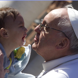 Papa Francesco accarezza e bacia un bambino che gli è stato allungato dalla folla in piazza San Pietro (Ansa)