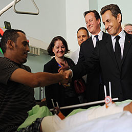 Sarkozy e Cameron in Libia: «Gheddafi è un pericolo» Farnesina: «Diplomazia non è rubabandiera». Nella foto il presidente francese Nicolas Sarkozy (a destra) e il primo ministro inglese, David Cameron, stringono la mano a uno dei feriti ricoverati presso l'ospedale di Tripoli, nel corso del loro viaggio in Libia (Epa)