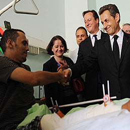 Sarkozy e Cameron in Libia: Gheddafi  un pericolo Farnesina: Diplomazia non  rubabandiera. Nella foto il presidente francese Nicolas Sarkozy (a destra) e il primo ministro inglese, David Cameron, stringono la mano a uno dei feriti ricoverati presso l'ospedale di Tripoli, nel corso del loro viaggio in Libia (Epa)