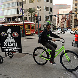 Un ciclista cerca di guadagnare qualche soldo con la pubblicità mobile della finale del Superbowl 2013 passeggiando per le strade affollate di New Orleans, Louisiana (Epa)
